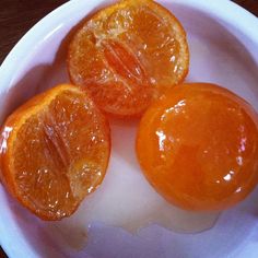 three peeled oranges sit in a white bowl on a wooden table, ready to be eaten