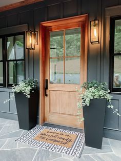 two large planters with plants are on the front steps of a house that has a welcome mat in front of it