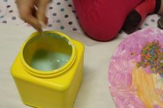 a child's hand is pouring water into a yellow container with sprinkles