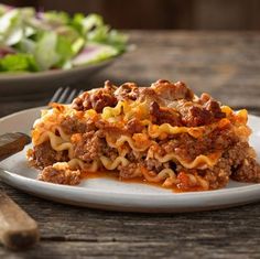 a white plate topped with lasagna next to a salad