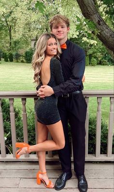 a man standing next to a woman on top of a wooden bench in front of a tree