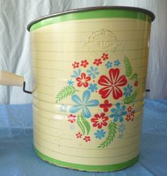 an old yellow and green flowered bucket on a blue tablecloth with a white wall in the background