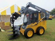 a yellow skid steer parked on top of a grass field next to a white tent