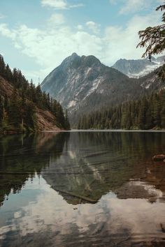 a lake surrounded by trees and mountains with clouds in the sky over it's surface