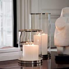 three white candles sitting on top of a table next to a vase and bookcase