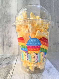 a plastic cup filled with yellow popcorn on top of a wooden table next to a white wall