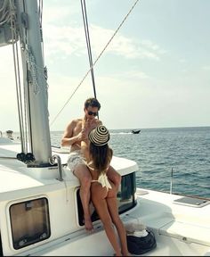 two people sitting on the back of a sailboat in the ocean, with one person wearing a hat