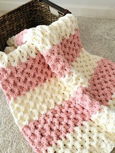 a pink and white crocheted blanket sitting on the floor next to a basket