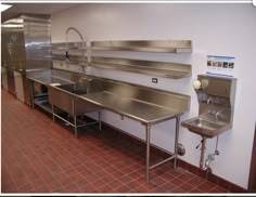 an industrial kitchen with stainless steel sinks and counter tops on the wall, along with red tile flooring