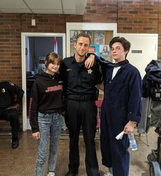 three people standing next to each other in front of a brick wall and two police officers