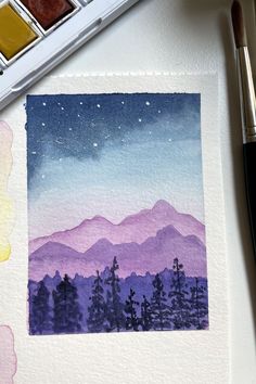 a watercolor painting of mountains and trees in the distance with paintbrushes next to it