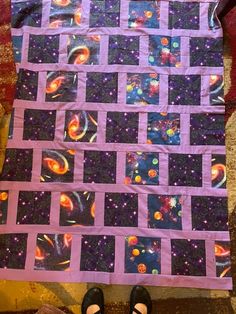 someone is standing next to a quilt made with space and stars in the background,