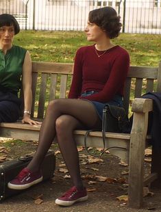 two women sitting on a wooden bench in the park, one with her legs crossed