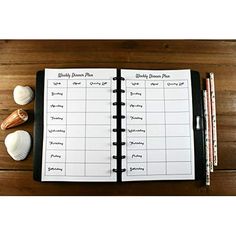 an open planner with seashells and pencils next to it on a wooden table