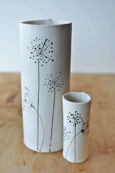 two white vases sitting on top of a wooden table next to each other with dandelions painted on them