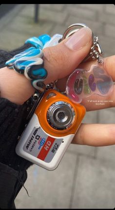 a person holding a small camera keychain in their left hand, with other items attached to it