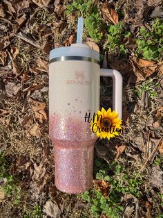 a pink and silver glittered tumbler with a sunflower on the ground next to it