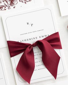 a close up of a red ribbon on a white card with flowers in the background