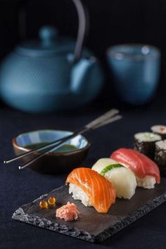 sushi is served on a slate plate with chopsticks