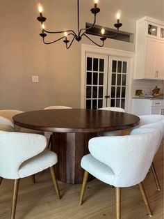 a dining room table with white chairs and lights hanging from the chandelier above it