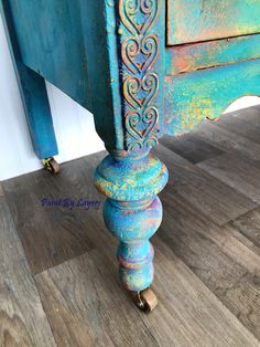 an old wooden table with blue paint and ornate carvings on the top, sitting on wood flooring