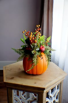 an orange pumpkin decorated with berries and greenery on a small wooden table in front of a window