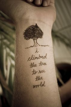 a hand holding up a tattoo that reads, i climbed the tree to see the world