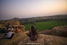 people are sitting on the rocks looking out over a green field and valley in the distance