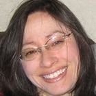 a woman wearing glasses and smiling at the camera while sitting next to a gray cat