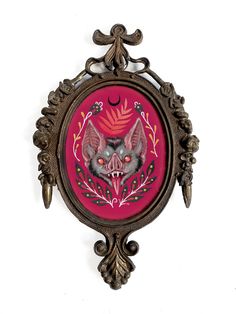 an ornate metal frame with a bat painted on it's face in pink and gold