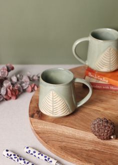 two mugs sitting on top of a wooden tray next to some pens and pencils