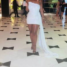 a woman in a short white dress standing on a tiled floor with her legs crossed