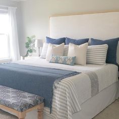 a large bed with blue and white pillows on it's headboard next to a window