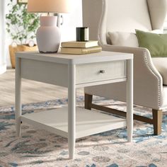 a white table with a lamp and some books on it in a living room next to a couch