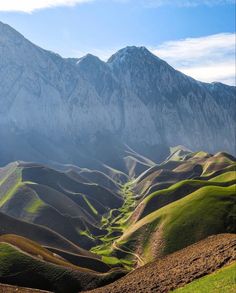 the mountains are covered in green grass and brown dirt, with some snow on them