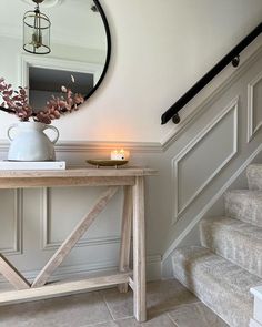 a table with a mirror and candle on it in front of some stairs that are painted white