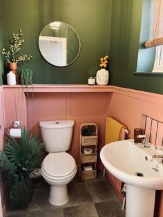 a white toilet sitting next to a sink in a bathroom under a mirror and potted plant