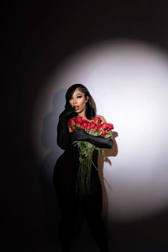 a woman holding flowers in her hands and posing for the camera with a black background