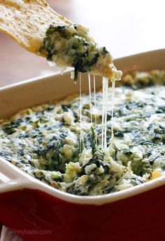 spinach dip being scooped from a red casserole dish with bread on the side