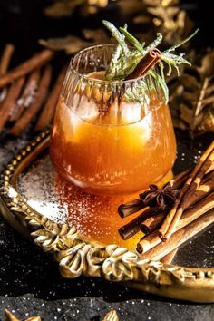 a glass filled with liquid and cinnamon sticks on top of a tray next to an assortment of spices