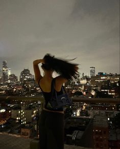 a woman standing on top of a building with her hair blowing in the wind at night