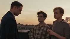 three men standing next to each other in front of a bridge with the sun setting