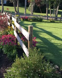 a wooden fence surrounded by flowers and trees in a park with lots of green grass