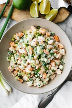 a white bowl filled with shrimp salad next to limes