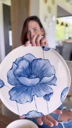 a woman holding a plate with blue flowers painted on it