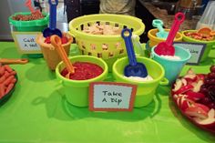 a table topped with bowls filled with food and plastic utensils on top of a green table cloth