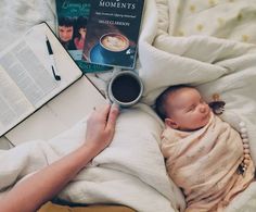 a woman holding a cup of coffee while reading a book with a baby in her lap