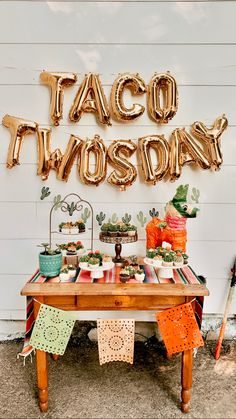 a taco themed birthday party with gold balloons and decorations on a wooden table in front of a white wall