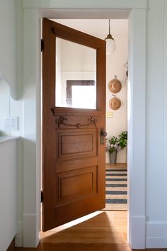 an open wooden door leading to a hallway with potted plants on the wall and light fixture