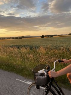 a person riding a bike down the road in front of a field with tall grass